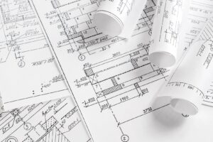 Several architectural blueprints with technical drawings and measurements, some flat and some rolled up, laid out on a white surface, showcasing professional Drafting Services.