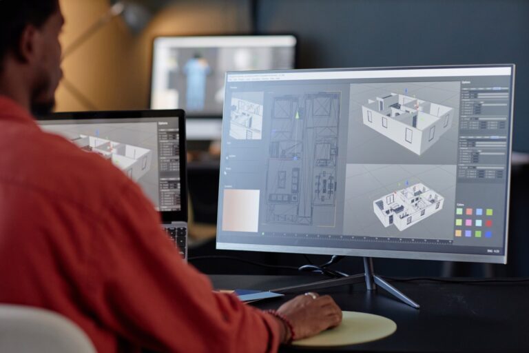 Person working at a desk with a computer displaying 3D architectural design software and floor plans on the screen, highlighting the precision of professional drafting services.